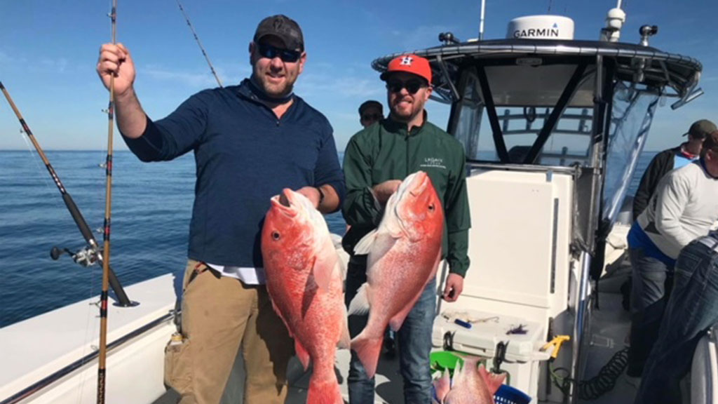 Two men on a Galveston deep sea fishing charter boat hold up the red snapper they just caught.