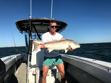 Man holds a large, bull redfish he just caught aboard a Galveston Bay & Jetty Fishing Charter.